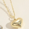 Detalle macro del colgante de corazón 3D pulido con acabado dorado brillante en cadena - Corazón bañado en oro de 14K / Dorado