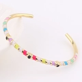 Detail of thin gold bracelet with colorful enamel stripes and black eye-shaped dots - Colorful