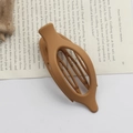 Brown matte oval hair claw clip with minimalist design placed on an open book - Matte Light Coffee