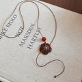 Détail d'un pendentif en bois fleuri avec perle rouge sur une cordelette tressée - Pendentif Fleur / Marron