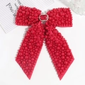 Detailed view of a red ribbon bow hair clip with faux pearls and a large center gemstone - Red