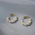 Elegantes pendientes de aro dorados retorcidos con pequeñas perlas blancas sobre tela gris - Dorado