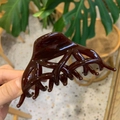 Dettaglio di un fermaglio per capelli in resina marrone rossastro scuro lucido in mano - Coda di Fenice a Farfalla / Cioccolato