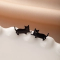 Detalle de pendientes de gato negro sobre plato de cerámica blanca y tela de seda suave - Negro