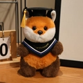 Volpe di peluche con tocco di laurea nero e fascia Congratulations su piano legno - Volpe con sciarpa blu / 20cm