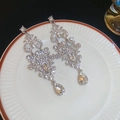 Exquisite silberne Tropfenohrringe mit funkelnden Strasssteinen auf weißem Keramikteller - Silber (Silberstift)