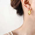 Dettaglio di eleganti orecchini a cerchio intrecciati dorati indossati da una modella - Forma C Intrecciata (Grande) / 3CM di diametro / Oro