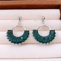 Macro shot of dark green pleated leather earrings with silver metal beads on a beige tray - Green