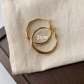 Dettaglio di orecchini a cerchio dorati da 3 cm presentati su un sacchetto in lino beige - 30MM / Oro