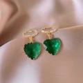 Dettaglio di orecchini a cuore verde placcati oro su tessuto di raso champagne - Verde