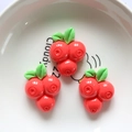 Detailed view of red resin raspberry charms with green leaves on a minimalist white plate - Red Berries