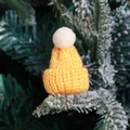 Mini yellow knitted Christmas hat with white pom-pom on snowy pine tree branch - Yellow