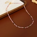 Detail shot of a sweet pink and white beaded necklace with a golden lobster clasp on wood - Gold-Pink