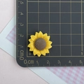 Dettaglio di un ciondolo a girasole in resina da 2,5cm su un tappetino millimetrato - Girasole Piccolo