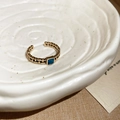 Detalle macro de un anillo de cadena dorado vintage con gema azul cuadrada - Estilo Cuadrado Dorado