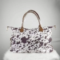 Close-up of cow print canvas weekender bag with brown handles and gold hardware - Brown Cow Print