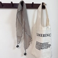Detail of grey triangle scarf with pom-poms hanging on a hook next to a canvas tote bag - Khaki