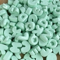 Vista macro di mini perline in resina verde chiaro a forma di lettere per decorazioni - Dolcetto o Scherzetto / Confezione singola casuale / Verde