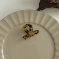 Detail of a large leopard print hair claw clip on a textured plate with branding text - Small Y-Shape Clip