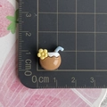 Dettaglio ravvicinato di mini ciondolo in resina a forma di cocco con misure su tappeto - Succo di Cocco con Fiore Giallo