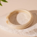 Detail van een amber marmeren acryl hars armband geplaatst op een witte minerale steen - Rijstwit Acryl Rond Bangle