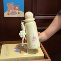 Detail of cream yellow cartoon thermos with bear print, floral pendant, and hand strap - Yellow Bear