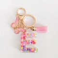 Detail of resin letter E keychain with pink sequins, butterfly charm and soft tassel - Letter E