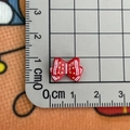 Close-up of a 1.2cm red resin bow charm with stripes on a centimeter scale mat - Bow