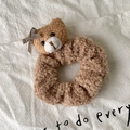Detailansicht eines braunen Plüsch-Teddybär-Haargummis mit Karo-Schleife auf weißem Stoff - Kaffee Teddy Samt Bär