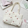 Close-up of quilted beige tote bag featuring red bow embroidery and front button pockets - Red Bow