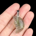 Green fluorite hand-carved crescent moon face pendant held for scale against black background - Fluorite