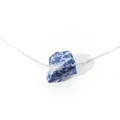 Macro shot of irregular blue raw stone pendant with silver chain on white background - Blue Sodalite