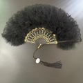 Close-up of black feather folding fan with gold hollow patterns and white flower pendant - Double-sided Lace Feather Fan Black