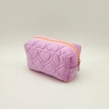 Pink plush pencil case with quilted heart pattern and orange zipper on white background - Purple