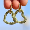 Orecchini a cuore placcati oro 18K con zirconi verdi tenuti contro lo sfondo del cielo blu - Verde