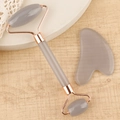 Close-up of grey resin facial roller and heart-shaped gua sha tool set on a wooden base - Resin Roller Transparent Grey