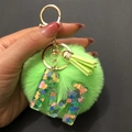 Detailed macro view of green pompom keychain with clear resin heart sequin letter A - Letter A