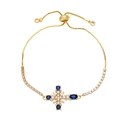 Bracciale a croce dorato regolabile con cristalli blu e perle su sfondo bianco pulito - Blu