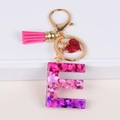 Close-up of glittery resin letter E keychain with pink tassel and heart pendant - Letter E