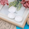 Three white floating tea light candles on a decorative floral background with pink petals - White