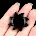 Black obsidian sun stone carving held in hand to demonstrate the small craft size - Obsidian