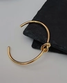 Makroaufnahme der goldenen Knot-Armspange auf minimalistischem Schieferhintergrund - Gold