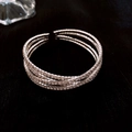 Detalle de brazalete plateado multicapa con pedrería brillante sobre madera - Plata-Cruz