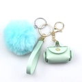 Dettaglio del pompon azzurro e mini borsa in pelle verde con cinturino portachiavi - Verde