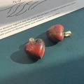 Macro shot of heart-shaped red-brown stone pendants with gold metal bail on green surface - Rhodonite
