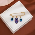 Detail of gold brooch with blue evil eye charms and Hamsa hand on white jewelry cushion - Triple Evil Eye Style (Z337-3)