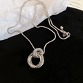 Detailopname van gelaagde zilveren cirkelhanger aan slangenketting op wit reliëfpapier - Zilver