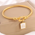 Gold twisted cable bangle with Libra zodiac charm and horseshoe clasp on jewelry box - Gold Libra
