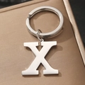 Polished silver metal letter X keychain with sturdy circular key ring on beige surface - Letter X