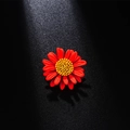 Elegant red enamel daisy brooch with a yellow core on a dark textured background - Red